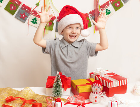 Joyful child boy in Santa red hat, surprised by Christmas gifts. Happy holidays