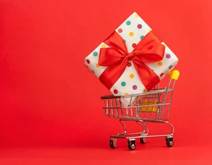 Fotobehang Winkelwagentje met kleurrijke cadeau op een rode achtergrond met plaats voor tekst. © Albert Ziganshin