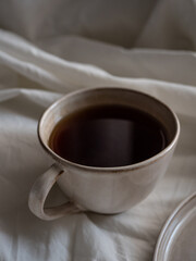 Breakfast in bed, a cup of black tea and thin pancakes with currant jam and sour cream on a beige ceramic plate on a soft white bed in the morning light
