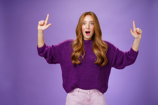 Guys It Cool You Cannot Imagine. Portrait Of Surprised And Impressed Excited Attractive Young Ginger Woman In Purple Sweater Raising Hands Pointing Up Dropping Jaw From Amazement Over Violet Wall