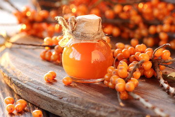 Sea buckthorn oil in glass bottle with fresh berries  on wooden rustic background, closeup, natural...