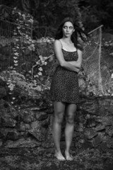 Black and white image of a young woman in flower print dress, exploring a woodland garden.