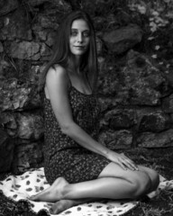 Black and white image of a young woman in flower print dress, exploring a woodland garden.