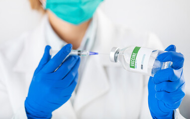 Close up of female doctor in face mask and gloves filling sterile syringe with vaccine from covid. Preparing drugs for vaccination at clinic.