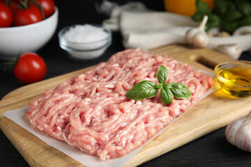 Raw chicken minced meat with basil on black wooden table, closeup