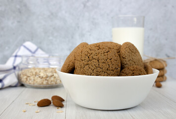 Oatmeal cookies in a white bowl and a glass of milk on a concrete background