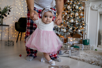 little girl makes her first steps with dad near the christmas tree