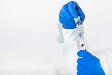 Close up of doctor hands in blue rubber gloves holding vaccine bottle and syringe. Medical worker preparing drugs for patient. Health treatment concept.
