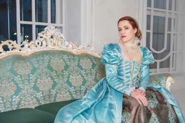 Beautiful woman in medieval style blue dress sitting on the sofa