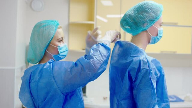 Female nurse on the clinic before to start a surgical operation helping to get dressed the doctor on the special equipment. 4k