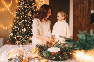 The concept of Christmas. Mom and little daughter child in cozy sweaters together prepare a festive cupcake meal in the decorated kitchen during the New Year holidays at home. Selective focus
