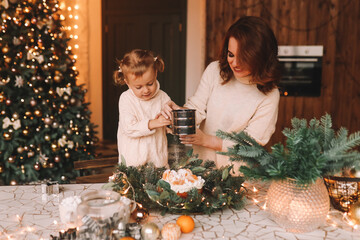 The concept of Christmas. Mom and little daughter child in cozy sweaters together prepare a festive cupcake meal in the decorated kitchen during the New Year holidays at home. Selective focus