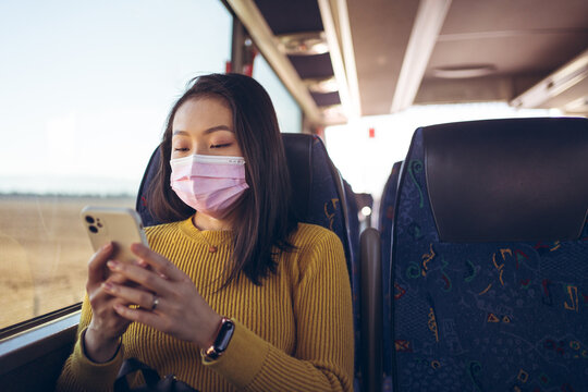 Young Asian Pretty Woman Travelling In Bus With Pink Mask Using Smartphone