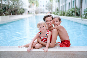 Fototapeta na wymiar Vacation with a family. Happy young mother and her kids having fun in swimming pool.
