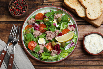 Plate of delicious salad with canned tuna and vegetables served served on wooden table, flat lay
