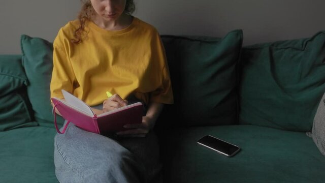 The girl makes notes in a notebook sitting on a bright sofa