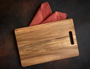 Cutting board on orange kitchen linen towel on dark kitchen table. Top view of a flat surface
