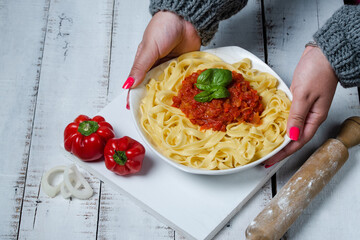 hands of young woman with plate of cooked noodles with tomato sauce