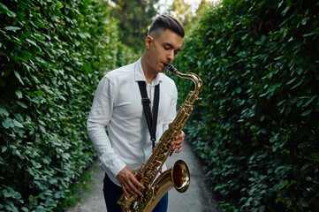 Male saxophonist plays on the alley in summer park
