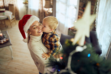 Fototapeta na wymiar Small boy kisses his mother by Christmas tree at home.