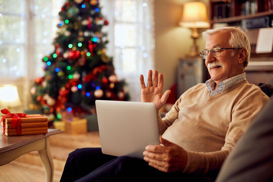 Happy senior man greets someone during video call on Christmas day at home.
