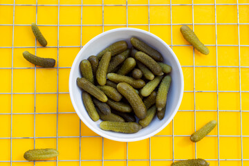 Pickled gherkins or cucumbers in bowl on yellow background.