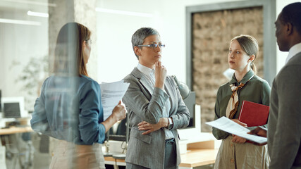 Female business leader listens to her co-workers while having briefing during team meeting at corporate office.