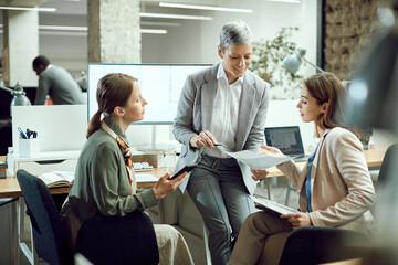 Female business team collaborate while analyzing reports on meeting at corporate office.