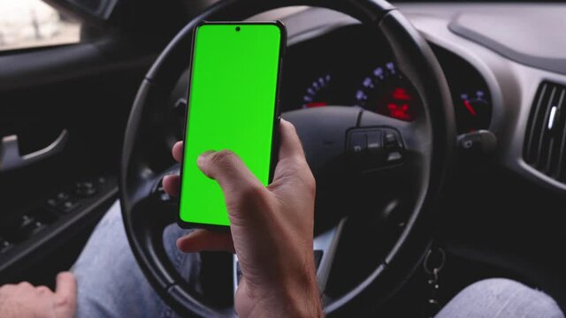 Using the phone while driving in the car. Phone with a green screen for your inscription. Copy space on your phone