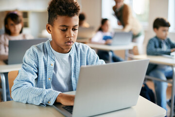 African American elementary student uses laptop on computer class in classroom.