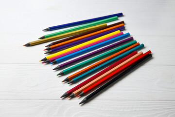 Multi-colored pencils on a white wooden background. Drawing set. School accessories.