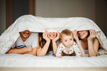 the family is at home in bed under a blanket, only smiles and a small baby are visible