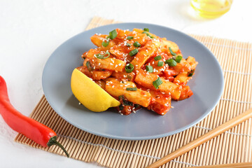 Plate with honey chilli potato and chopsticks on light background