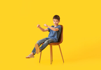 Little boy with imaginary steering wheel sitting in chair on color background