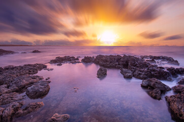 Long exposure sea sunset, blurry clouds, coastal stones.