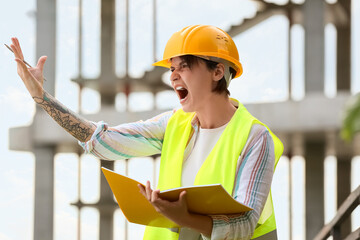Angry female construction worker in hardhat with folder outdoors