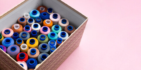 A set of colored sewing threads in a box on a pink background. View from above.