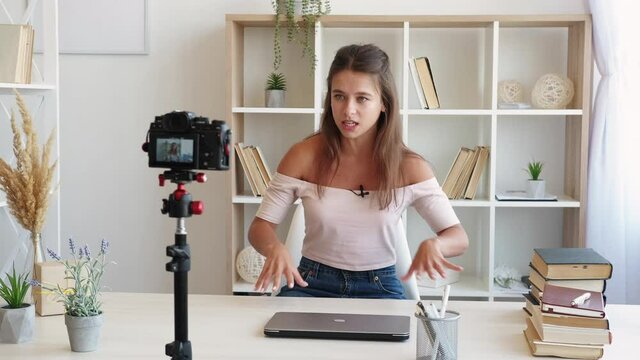 Female influencer. Life blog. Video conference. Happy stylish woman talking expressive on photo camera in light room interior.