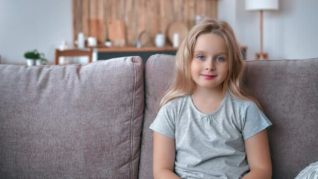 Portrait of happy little blonde girl with natural beauty smiling relaxing weekend sitting on couch