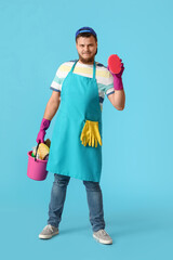 Young man with cleaning supplies on blue background