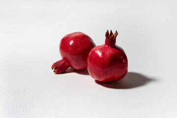 Still life with grenades. Two ripe fruits lie on a white textured background, illuminated by harsh light.