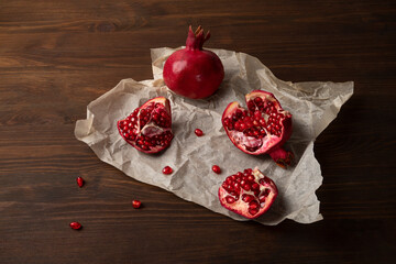 Pieces of ripe pomegranate lie on parchment paper. Wooden background, horizontal orientation, close-up, top view. 