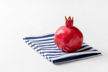 Pomegranate lies on a folded striped towel. White textured background, horizontal orientation, copy space.