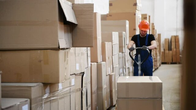 Young male worker in uniform is in the warehouse pusing pallet truck