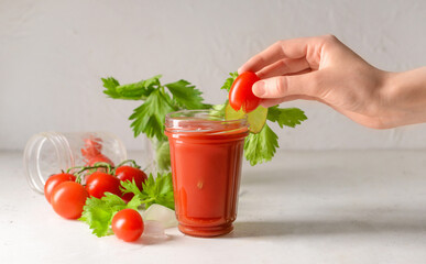 Woman decorating glass of bloody mary with cherry tomato at table