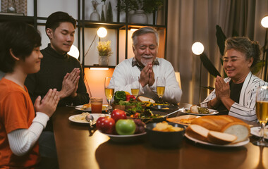 Asian big family closing eyes and praying hands when saying grace praying before having dinner at home