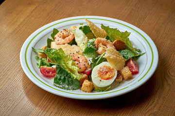 Caesar salad with shrimp and parmesan in a white plate on a wooden background