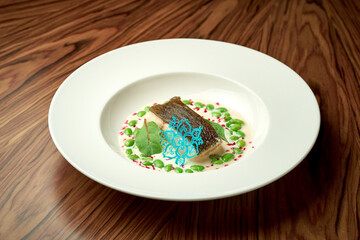 Black cod fillet with edem beans and white sauce in a white plate on a wooden background