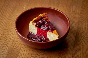 Cheesecake with berry sauce in a clay plate on a wooden background