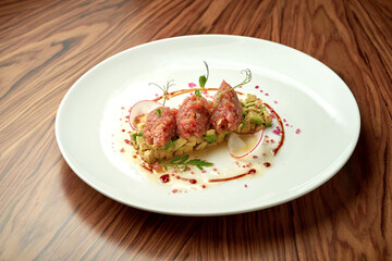 Tuna tartare with avocado and sauce in a white plate on a wooden background